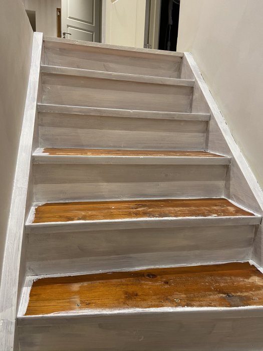 Trappa under renovering med grundmålad vit panel och omålade trästeg.