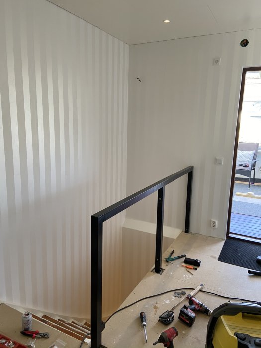 Ej färdigmonterat svart räcke i ett rum under renovering, verktyg och byggmaterial på golvet.
