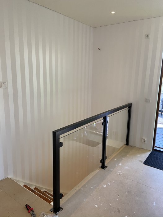 Räcke med glas och svarta metallstolpar på en byggplats, monterat men inte färdigställt.