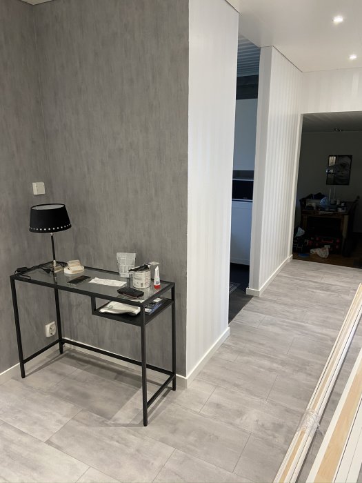 Modern inredning med grått klinkergolv, vita golvlistar och dörrfoder framför en tapetserad vägg med skrivbord.