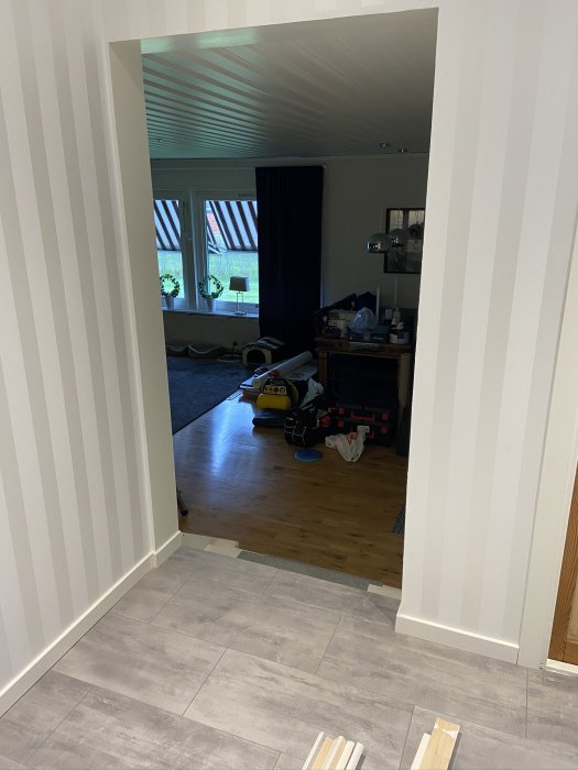 Dörröppning med nyinstallerade vita golvlist och foder som förbinder ett rum med grå klinker och ett annat med trägolv.