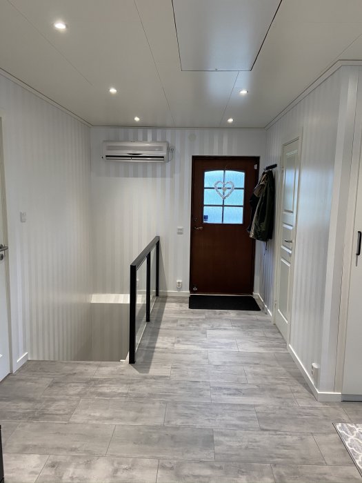 Renoverat rum med vit panel, grått golv, luftkonditionering och en brun ytterdörr med hjärtdesign.