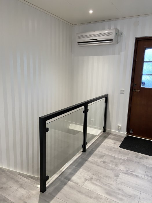 Nyligen renoverat rum med vit randig tapet, luftkonditionering och svart räcke vid trappa.