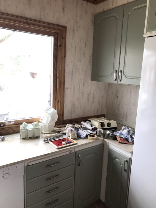 Kök före renovering med stökiga bänkytor, öppna skåp och renoveringsmaterial utspritt.