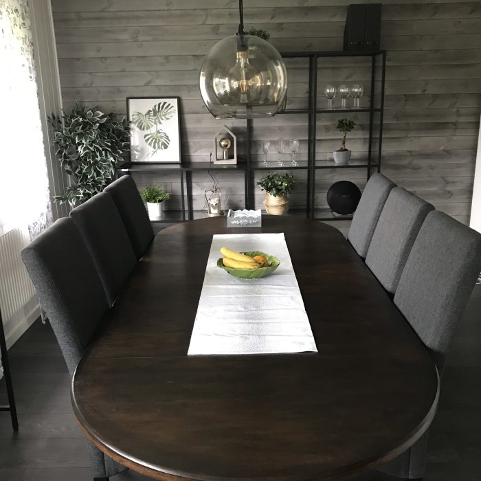Modern matsal med träbord, gråa stolar och inredningsdetaljer, ugnen ej synlig.