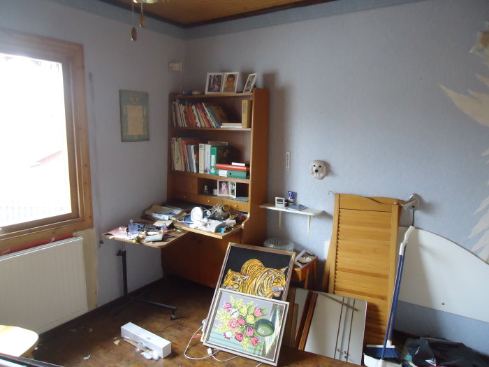 Oorganiserat sovrum före renovering med möbler och föremål utspridda.