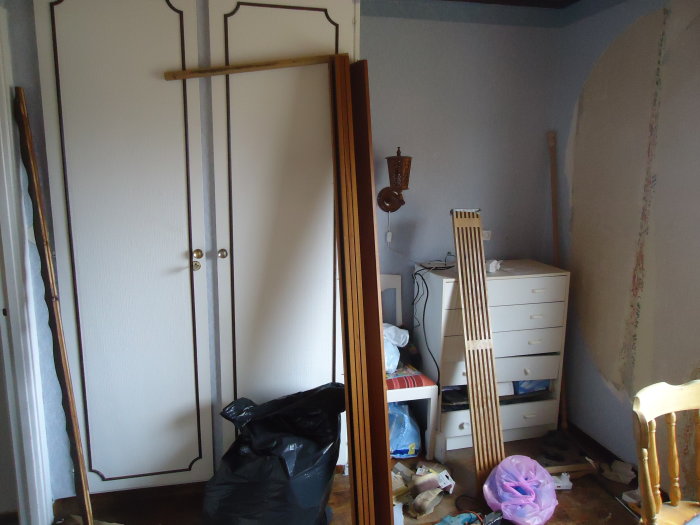 Ostädad sovrumsbild under renovering med garderober, byrå och byggmaterial.