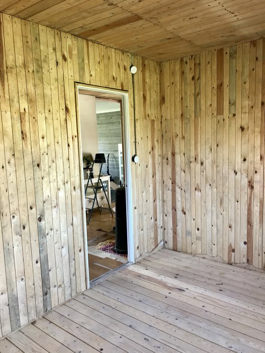 Rum helt klätt med träpanel på väggar och i taket, samt synligt trägolv, med öppen dörr till nästa rum.