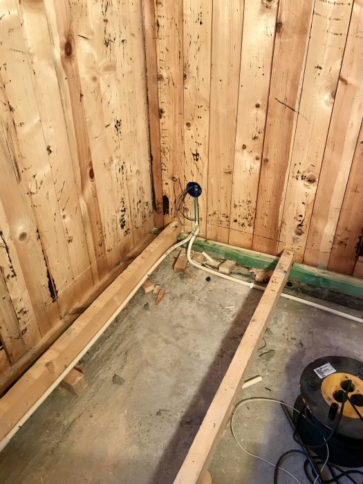 Inre hörn av ett rum under renovering med träväggar och elinstallationer, redo för isolering.