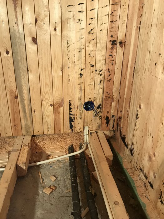 Färdigdragen el i ett träväggshörn med utstickande elrör och obehandlat golvråspår redo för isolering.