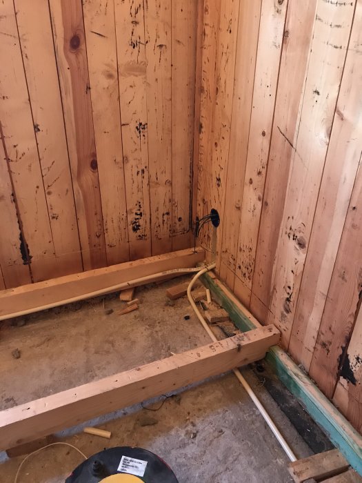 Hörn av ett rum under renovering med färdigdragna elkablar och osolerade träväggar.