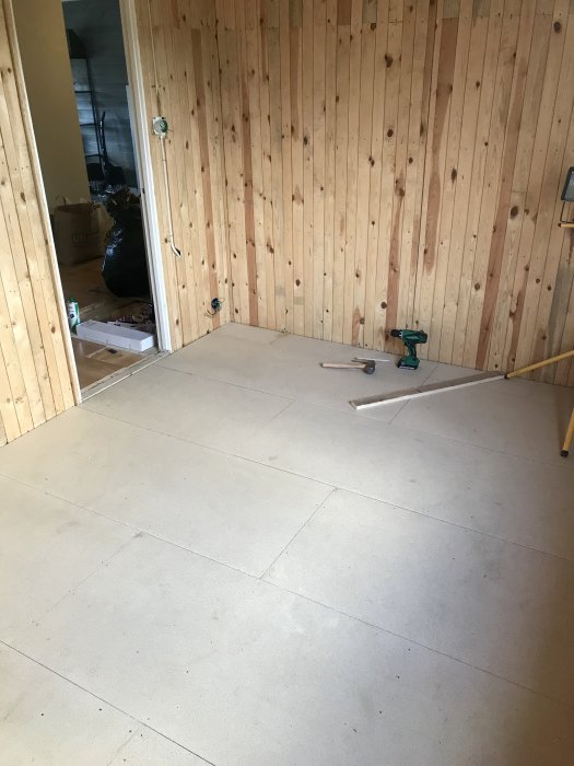 Installation av golvspånplattor i ett rum med träväggar och verktyg på golvet.