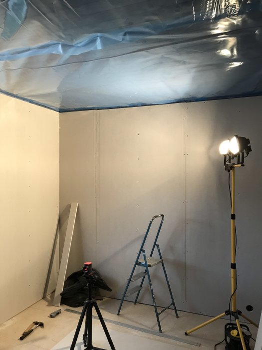 Renoveringsarbete med gipsväggar och byggplast i taket, stege och verktyg synliga.