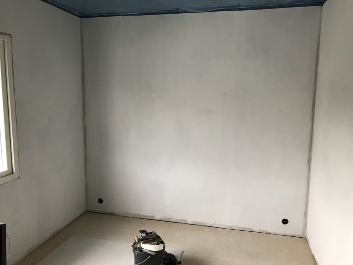 Rum under renovering med gipsskivor på väggarna och byggplast längs kanten av taket.