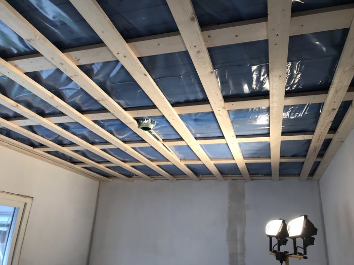Innertak under konstruktion med läkt och isoleringsmaterial, laser för riktning framgår i rum.