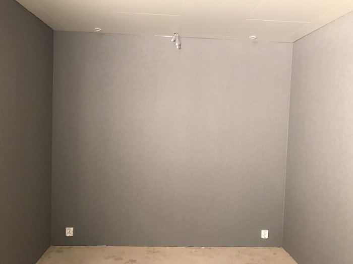 Nyttapetserad hörnvägg och installerat vit innertak i ett renoverat rum.