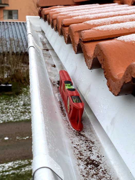 Vattenpass visar fel lutning på en hängränna med snö på takpannor i bakgrunden.