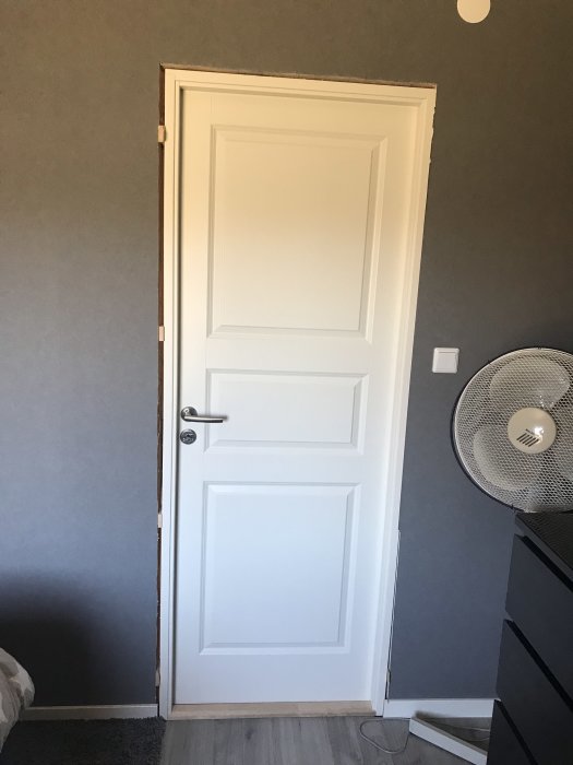 Ny vit innerdörr med tre vertikala paneler, installerad i ett grått rum med synlig dörrkarm.