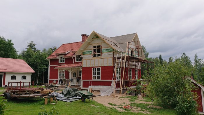 Renovering av en röd villa med pågående arbete på fasaden och ställningar runt huset.