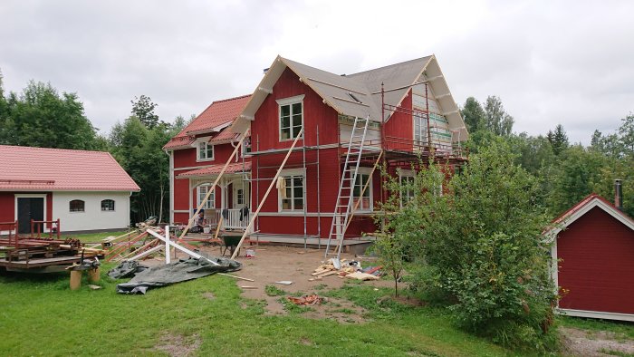 Renovering av rödmålat hus med ställningar och pågående panelspikning, omgiven av byggmaterial.