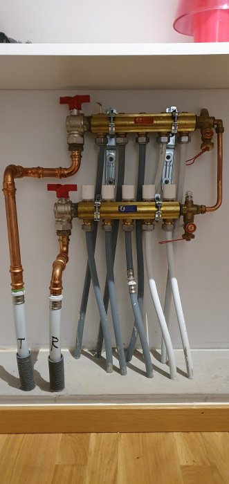 Golvvärmedistributionsblock med justerbara ventiler och kopplade rör för luft/vatten värmesystem.