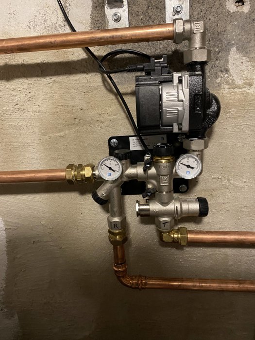 Golvvärmesystem med cirkulationspump, fördelarshunt och mätare på en vägg.