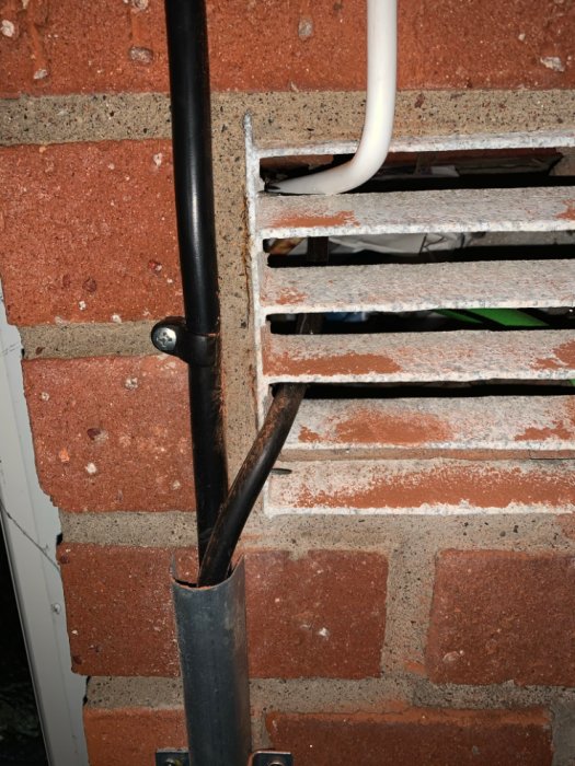 Elkablar dragna genom ett ventilationsintag i en tegelvägg med synlig isolering och rörgenomföring.