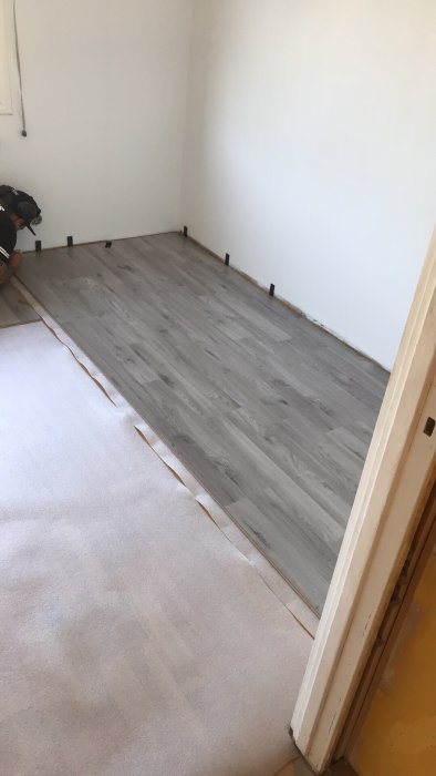 Installationsprocess av grått laminatgolv med vita väggar och lister.
