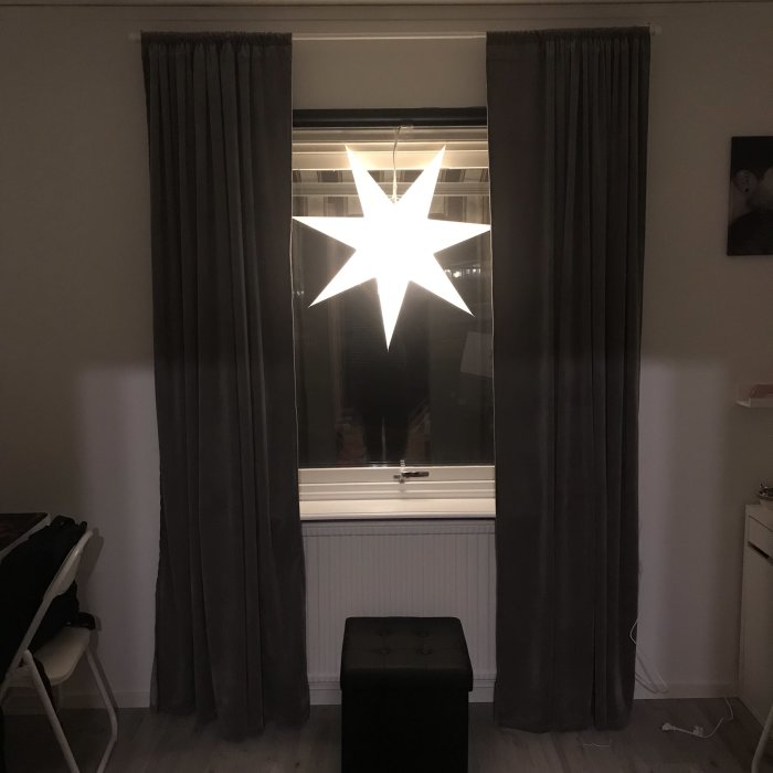 Renoverat rum med fönster dekorerat med en stjärnlampa, mörka gardiner och en svart pall.