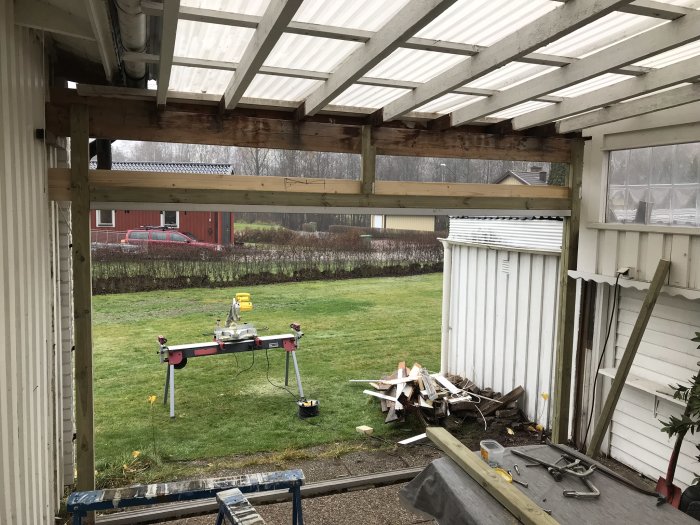 Renovering pågår i ett uterum med synligt träarbete, verktyg och skräp på golvet, utsikt över trädgården.
