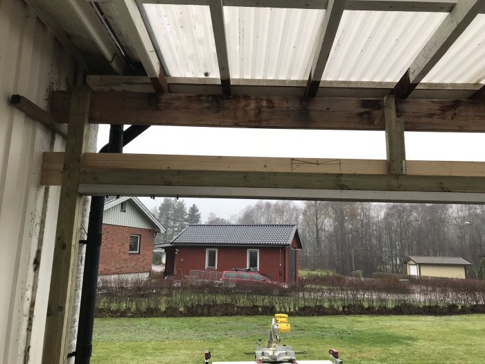 Utsikt från ett uterum under reparation med nya och gamla träbjälkar mot bakgrund av en röd stuga.