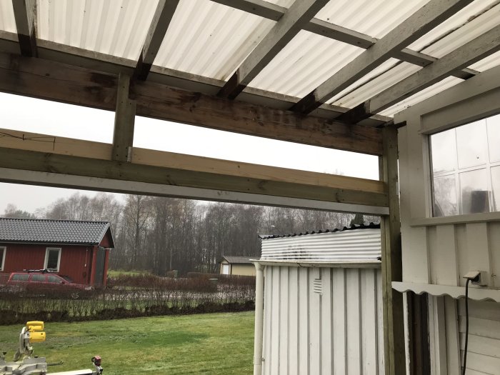 Renoverat takstöd i ett uterum med synligt timmer och skjutpartier, med en trädgård och röd byggnad i bakgrunden.