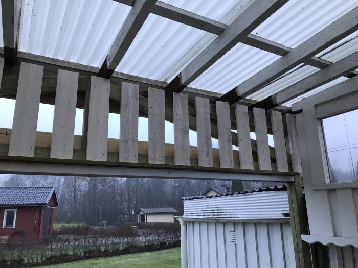 Träkonstruktion med öppningar som väntar på panelbeklädnad under tak av genomskinlig plast.