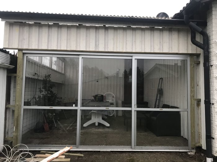 Vitmålad byggnad med stora fönsterpartier och synliga byggmaterial framför som indikerar pågående arbete.