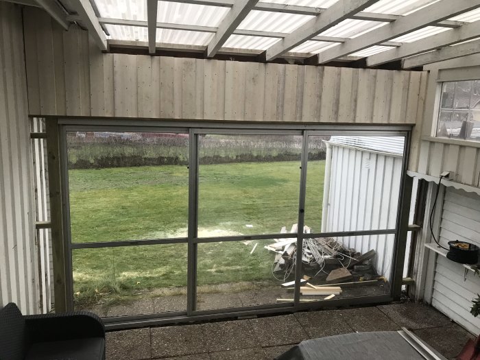 Vitmålad veranda med stora fönster och utsikt över en grön gräsmatta med byggmaterial synligt utanför.