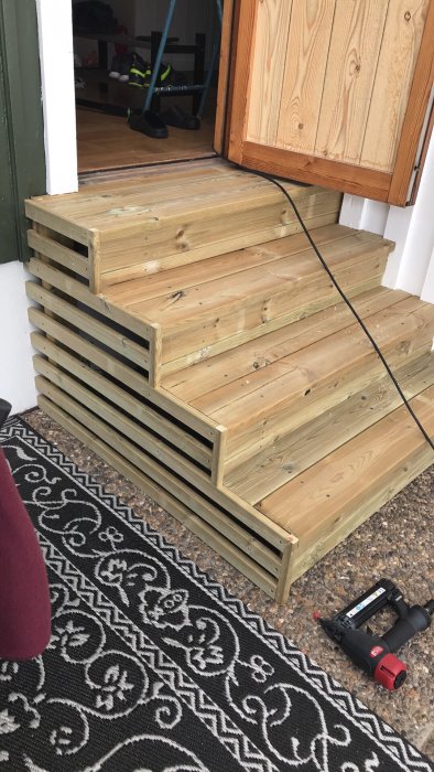 Nybyggd trätrappa utanför en dörröppning med verktyg på sidan.