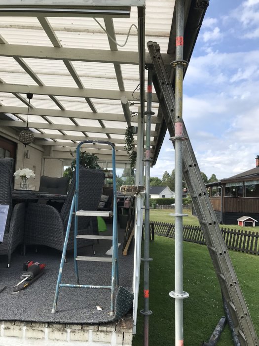 Ställningsmaterial används som stöttor för en terrass under renovering, med trädgårdsmöbler och verktyg synliga.