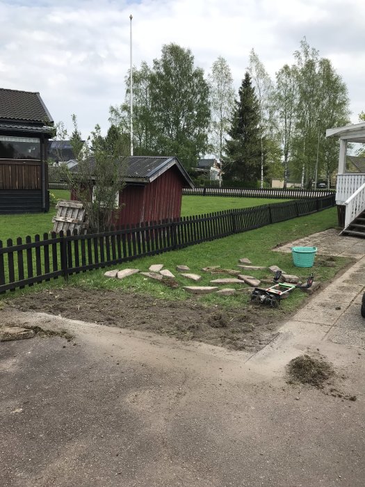 Uppgrävd gammal rabatt med borttagna plattor och en gräsklippare, redo för grässådd i trädgård.