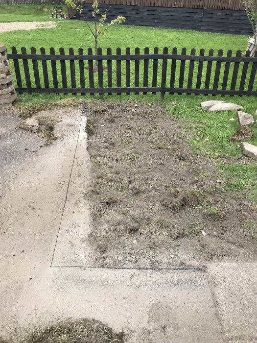 Nygrävd trädgårdsyta där en gammal rabatt varit, med staket och gräs i bakgrunden.