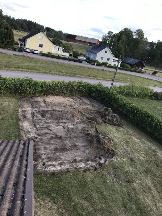 Schaktad mark på trädgård där gräsmatta har tagits bort, med hus och landskap i bakgrunden.