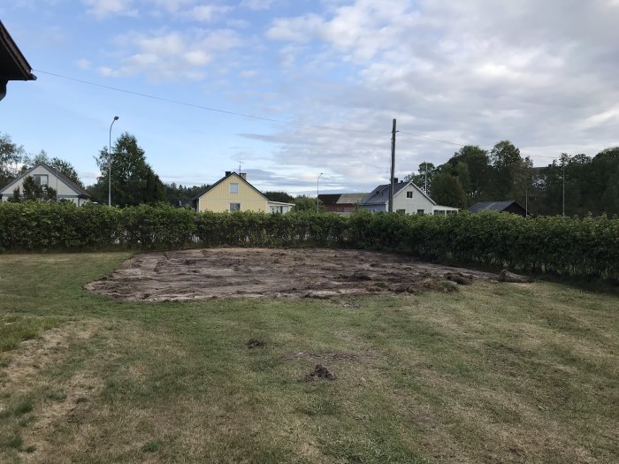 Ett schaktat område på en gräsmatta där tidigare ett växthus och potatisland legat, omgivet av grönt och hus.