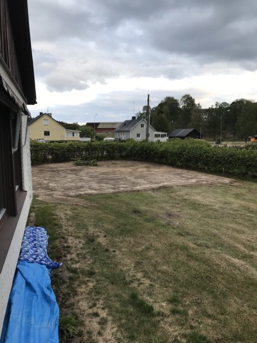 En ojämn gräsmatta med bar jord efter borttaget potatisland och växthus bakom ett hus.