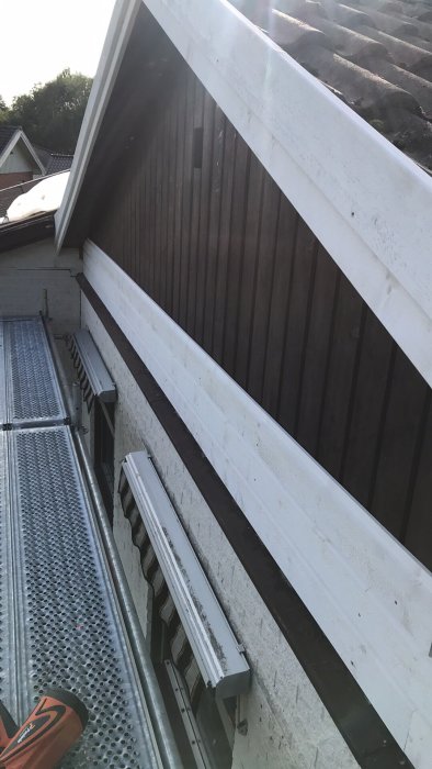 Bytt fasadpanel på hus med ny liggande vit panel ovanför gammal brun stående panel.