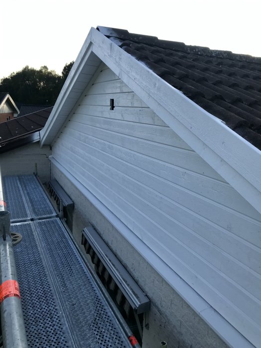 Ny målad vit fasad på ett hus med taktegel och byggställningar.