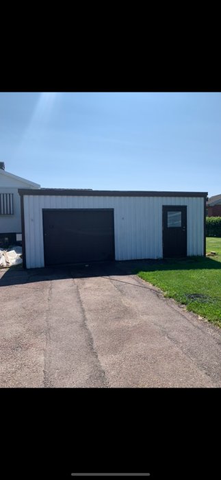 Nymålat grått garage med svart garageport och sidodörr, klarblå himmel ovanför.