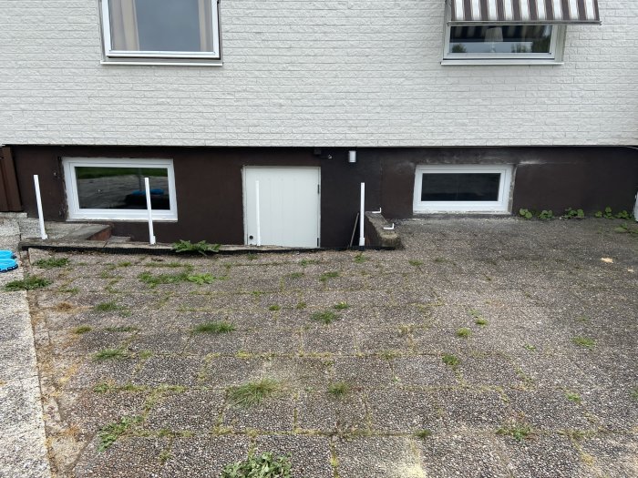 Nyinstallerad vit källardörr med skärmtak och en närliggande källarfönster på ett hus.