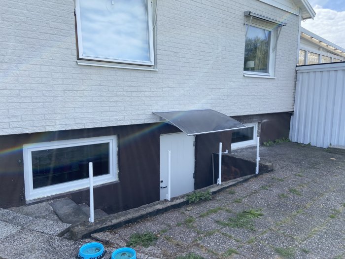 Nyinstallerad källardörr med skärmtak på husets sidovägg.