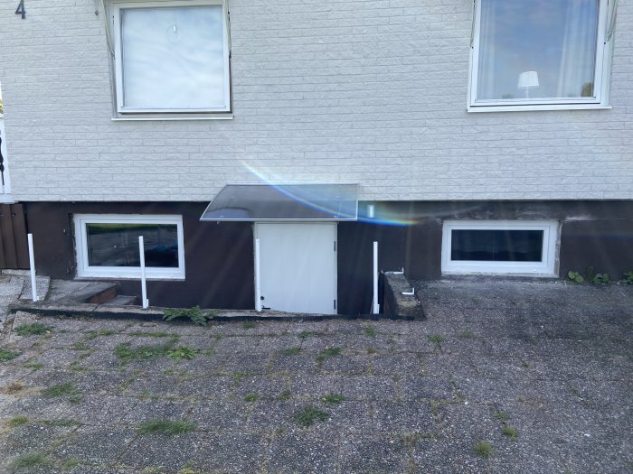 Ny källardörr med skärmtak och närliggande källarfönster på ett hus.