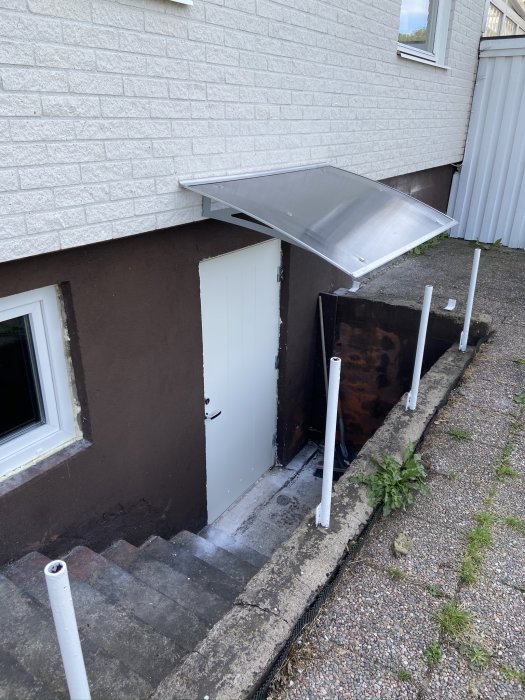 Nyinstallerad vit källardörr med skärmtak i metall ovanför, monterat på husets tegelvägg.