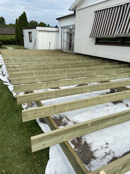 Nybyggd tom trästomme till ett däck intill ett hus, redo för räcken och trall, med snörester på marken.